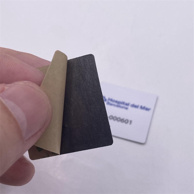 Close de uma mão retirando o liner de uma etiqueta RFID de PVC para superfícies metálicas, mostrando a camada adesiva pronta para fixação em equipamentos metálicos.