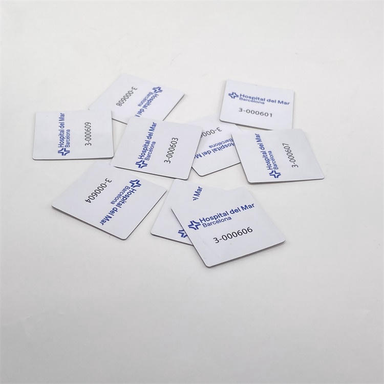Várias etiquetas RFID quadradas de PVC para superfícies metálicas estão espalhadas sobre um fundo branco, mostrando logotipos impressos e números de série nas superfícies acabadas.