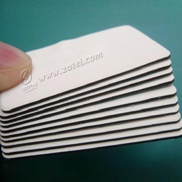 Vista aproximada de etiquetas RFID antimetal em PVC empilhadas, com cantos arredondados e estrutura isolante em camadas sobre uma superfície azul-petróleo.