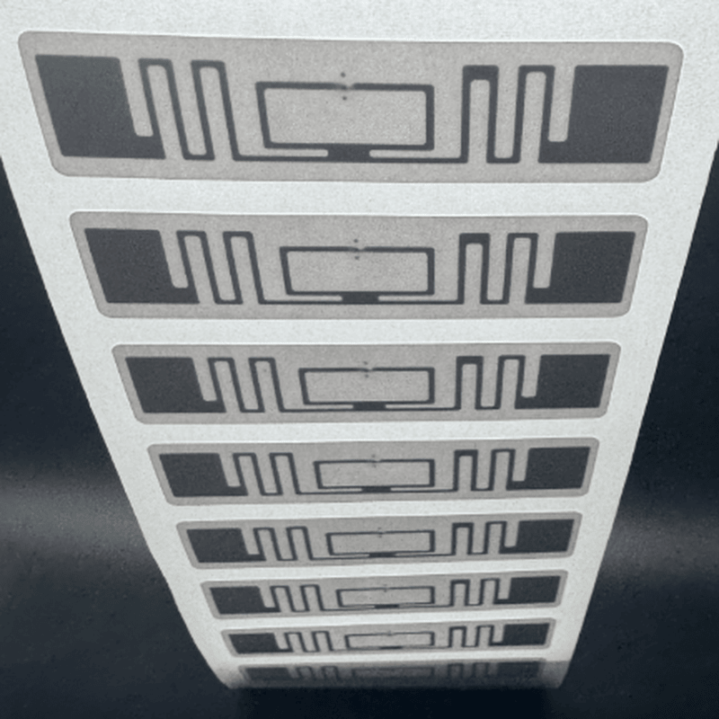 Foto em close mostrando uma tira de inlays de etiquetas RFID UHF de 70x15mm, preparada para codificação e triagem logística de alto rendimento.